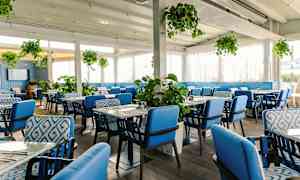 Ravintolan sisätila, jossa on sinisiä tuoleja ja vihreitä kasveja. (Tekoälyn luoma teksti)