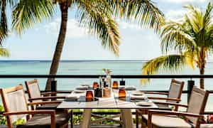 Kattaus pöydällä terassilla, josta on näkymä merelle ja ympäröiville palmuihin. (Tekoälyn luoma teksti)