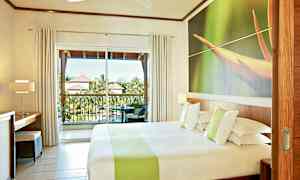 Hotellihuone, jossa on parisänky, suuri ikkunaseinä ja parveke, jolta on näkymä vehreään ympäristöön ja läheisten rakennusten katoille. (Tekoälyn luoma teksti)