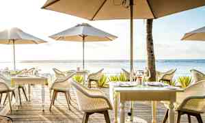 Ulkoilmaravintola, jossa on pöytiä ja aurinkovarjoja meren rannalla. (Tekoälyn luoma teksti)