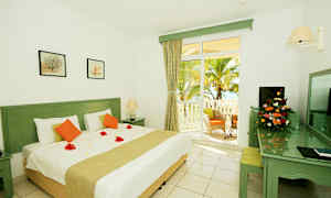 Valkoinen huone, jossa iso sänky, koristeellisia kukkia peitolla ja terassin ovi näkymineen palmupuutarhaan. (Tekoälyn luoma teksti)