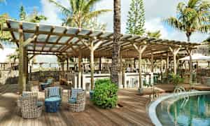 Trooppisen lomakeskuksen loungessa uima-altaan vieressä on istuimia ja baari puurakenteiden alla. (Tekoälyn luoma teksti)