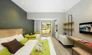 Moderni hotellihuone, jossa on sänky, työpöytä, sohva ja näkymä puutarhaan. (Tekoälyn luoma teksti)