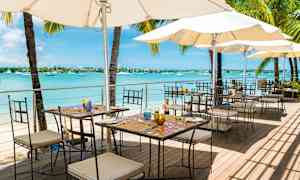 Ulkoterassi meren rannalla pöytien, tuolien ja aurinkovarjojen kanssa. (Tekoälyn luoma teksti)