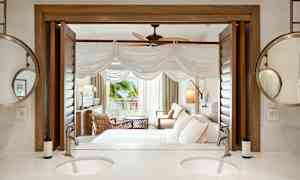 Hotellihuone, jossa istuinryhmä, sänky ja aukko verannalle. Etualalla näkyy kylpyhuone, jossa kaksinkertainen pesuallas ja peili. (Tekoälyn luoma teksti)