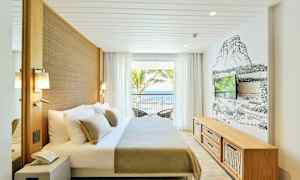 Valoisa hotellihuone, jossa on parivuode, seinään kiinnitetty televisio ja suuret ikkunat merelle päin. (Tekoälyn luoma teksti)