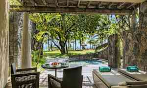 Terassi, jossa on istuimia ja aurinkotuoleja pienen altaan vieressä, ympäröitynä kasveilla ja näkymällä rannalle ja palmuihin. (Tekoälyn luoma teksti)