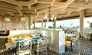 Moderni ravintola, jossa on geometrisesti kuvioitu lattia, vaaleat huonekalut ja suuret maisemaikkunat merinäköalalla. (Tekoälyn luoma teksti)