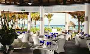 Ravintola, jossa on valkoiset punotut kalusteet katon alla ja näkymä merelle ja palmuihin. (Tekoälyn luoma teksti)