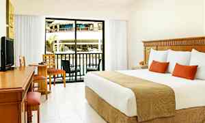 Hotellihuone, jossa on suuri sänky, työpöytä ja oleskeluryhmä. Lasinen ovi johtaa parvekkeelle, josta on näkymä allasalueelle. (Tekoälyn luoma teksti)