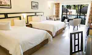 Kuva hotellihuoneesta, jossa on kaksi suurta sänkyä, istuma-alue ja pöytä suurten ikkunoiden edessä, jotka avautuvat uima-altaalle. (Tekoälyn luoma teksti)