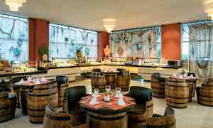 Ravintola-alue, jossa on tynnyrituolit ja -pöydät, buffetpöytä ja koristeltuja verhoja ympärillä. (Tekoälyn luoma teksti)