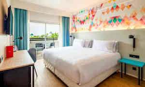 Hotellihuone, jossa on parivuode, värikäs seinäsuunnittelu, kirjoituspöytä ja parveke kahdella tuolilla. (Tekoälyn luoma teksti)