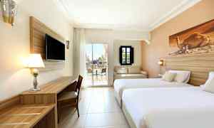 Hotellihuoneen kuva, jossa on kaksi sänkyä, TV, työpöytä ja istuinryhmä sekä näkymä terassille. (Tekoälyn luoma teksti)