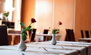 Tyylikkäästi katettu ruokapöytä, joka on koristeltu valkoisella maljakolla, joka sisältää yhden punaisen ruusun. (Tekoälyn luoma teksti)