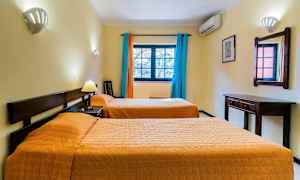 Hotellihuone, jossa on kaksi erillistä sänkyä, seinäpeili, kirjoituspöytä ja ikkuna värikkäillä verhoilla. (Tekoälyn luoma teksti)