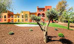 Rakennukset, jotka on maalattu keltaisella ja punaisella ja varustettu arcadeilla, ympäröivät puita ja maisemoituja viheralueita. (Tekoälyn luoma teksti)