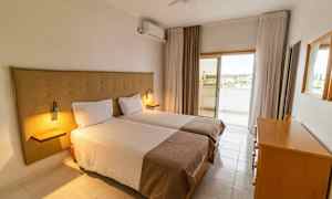 Hotellihuone, jossa on kaksi yhden hengen vuodetta, lipasto ja pääsy parvekkeelle. (Tekoälyn luoma teksti)