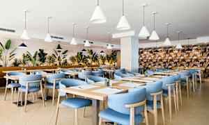 Ravintola, jossa on sinisiä tuoleja ja puupöytiä, ympäröitynä kasveilla. (Tekoälyn luoma teksti)