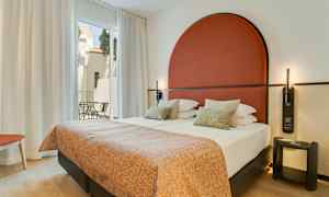 Moderni hotellihuone, jossa parivuode, punainen pääty ja suuret ikkunat parvekkeelle. (Tekoälyn luoma teksti)