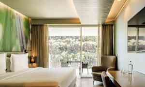 Hotellihuone, jossa on parivuode, istuinryhmä, pöytä tuoleineen sekä suuri lasiovi, joka avautuu parvekkeelle ja tarjoaa näköalaa luontoon ja kallioihin. (Tekoälyn luoma teksti)