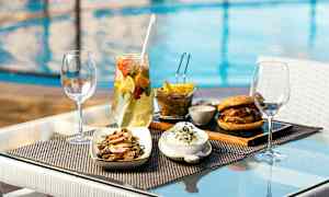 Ruokaa pöydällä altaan äärellä, sisältäen salaattia, hampurilaisen, ranskalaiset ja juoman. (Tekoälyn luoma teksti)