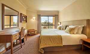 Kuva hotellihuoneesta, jossa on parivuode, työpöytä ja tuoleja sekä parveke näkymällä. (Tekoälyn luoma teksti)