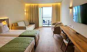 Hotellihuone, jossa kaksi sänkyä, sohva, kaksi nojatuolia, kirjoituspöytä ja parveke näkymällä. (Tekoälyn luoma teksti)