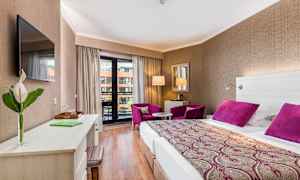 Hotellihuone, jossa on parivuode, kirjoituspöytä, kaksi violettia nojatuolia ja parveke. (Tekoälyn luoma teksti)