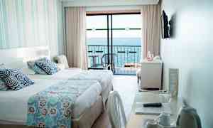 Hotellihuone, jossa on sänky, kirjoituspöytä ja näkymä merelle parvekkeelta. (Tekoälyn luoma teksti)