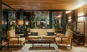 Sisätila, jossa istuinryhmä, joka koostuu sohvasta ja nojatuoleista lasiseinän edessä, ulkona näkyy kasvillisuutta. (Tekoälyn luoma teksti)