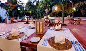 Valaistu ulkoilmaravintola katetuilla pöydillä ja palmuja taustalla. (Tekoälyn luoma teksti)