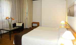 Hotellihuone, jossa on kaksi vuodetta, nojatuoli ja pöytä kukkamaljakolla. (Tekoälyn luoma teksti)