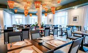 Ravintola, jossa on katettuja pöytiä ja moderneja tuoleja, ja katossa oransseja lamppuja. (Tekoälyn luoma teksti)