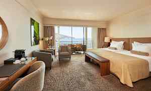 Hotellihuone, jossa on parivuode, istuinryhmä ja parveke merinäköalalla. (Tekoälyn luoma teksti)