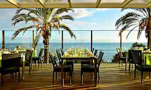 Ravintolapöytiä terassilla, näkymä merelle ja palmuihin. (Tekoälyn luoma teksti)