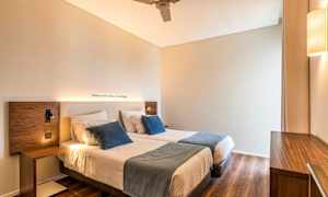 Huone, jossa on kaksi yhden hengen vuodetta, koristetyynyjä ja puiset sisustusmateriaalit. (Tekoälyn luoma teksti)