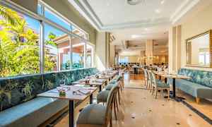 Valoisa ravintola, jossa on nykyaikaisia pöytiä ja tuoleja sekä suuret ikkunat, joiden kautta avautuu näkymä vehreään maisemaan. (Tekoälyn luoma teksti)