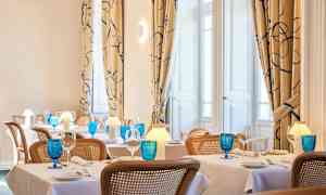 Kuva tyylikkäästä ravintolasta, jossa on katettuja pöytiä, siniset lasit ja lämmin valaistus. (Tekoälyn luoma teksti)