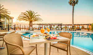 Aamiaispöytä uima-altaan äärellä, taustalla aurinkotuoleja ja palmuja. (Tekoälyn luoma teksti)