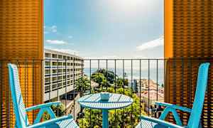 Kaksi sinistä tuolia ja pöytä parvekkeella, josta on näkymä merelle ja ympäröiviin rakennuksiin. (Tekoälyn luoma teksti)