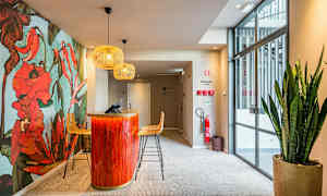 Vastaanotto, jossa koristeellinen kukkaseinä, puna-oranssi vastaanottotiski ja istuimet, yläpuolella nykyaikaisia valaisimia. (Tekoälyn luoma teksti)