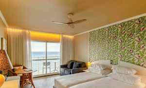 Hotellihuone, jossa on kaksi sänkyä, kuvioitu vihreä tapettiseinä ja parveke merinäköalalla. (Tekoälyn luoma teksti)