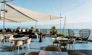 Ulkoterassi, jossa pöytiä ja tuoleja, pergola ja merinäköala. (Tekoälyn luoma teksti)