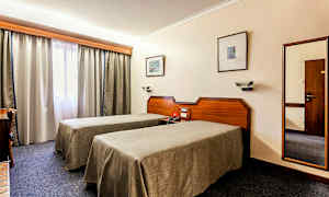 Kuva hotellihuoneesta, jossa on kaksi yhden hengen vuodetta, työpöytä ja ikkuna verhoineen. (Tekoälyn luoma teksti)