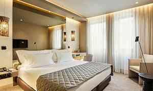 Modernisti sisustettu hotellihuone, jossa on parivuode, seinään kiinnitetty televisio ja suuret ikkunat vaaleilla verhoilla. (Tekoälyn luoma teksti)