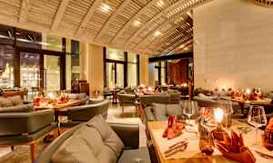 Tyylikäs ravintola, jossa on palkkikatto, katetut pöydät oransseilla lautasliinoilla ja kodikasta valaistusta. (Tekoälyn luoma teksti)