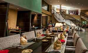 Tyylikäs ravintola, jossa pöydät ovat katettu lautasliinoilla ja lautasilla, sekä taustalla portaat. (Tekoälyn luoma teksti)