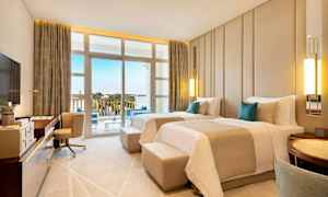 Hotellihuone, jossa on kaksi yhden hengen vuodetta, kirjoituspöytä, nojatuoli ja parveke näkymällä ympäristöön. (Tekoälyn luoma teksti)