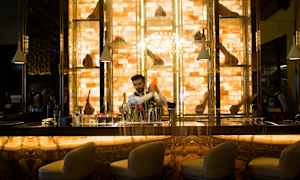 Kauniisti valaistu baaritiski, jonka edustalla on tuoleja ja taustalla hyllyjä koristeineen. (Tekoälyn luoma teksti)